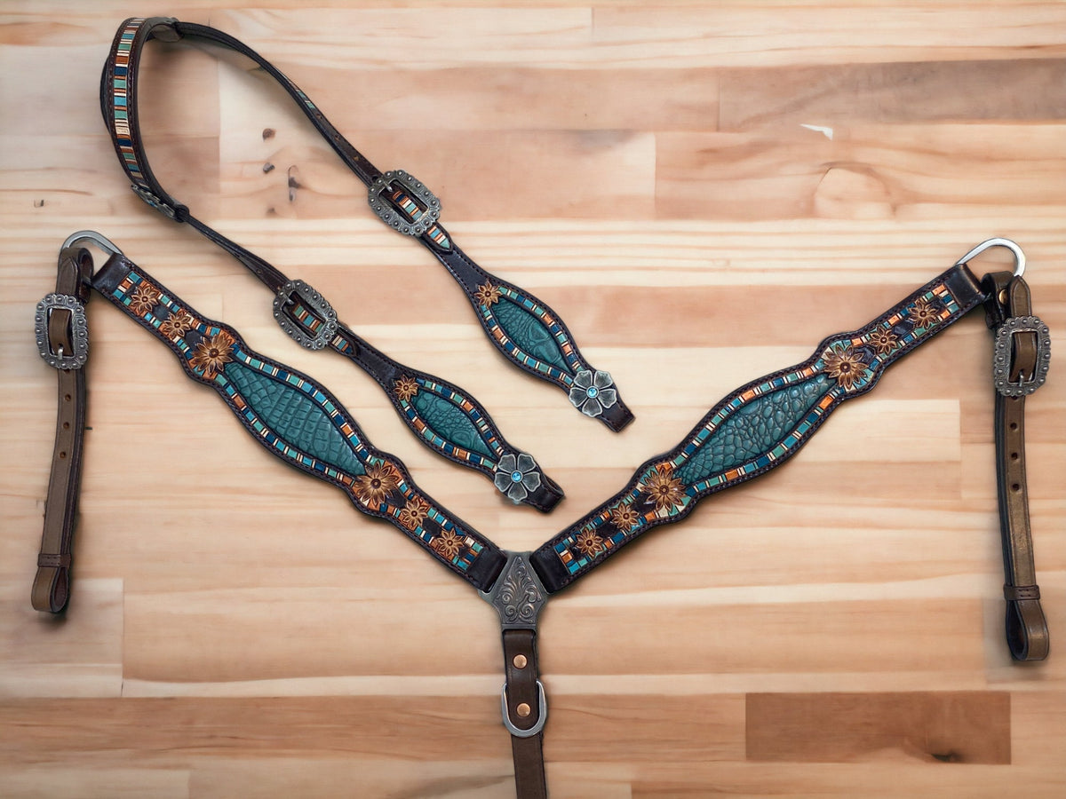 A complete Western horse tack set laid out on a wooden surface, featuring a teal alligator design with hand-tooled flower craving and antique copper hardware.