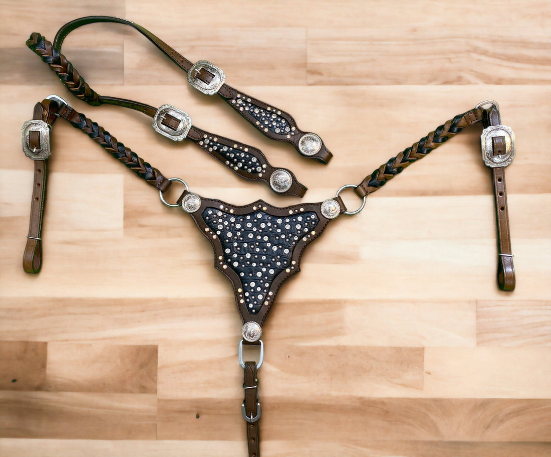 A cow leather headstall and breast collar set with black alligator pattern, clear rivets, and silver studs on a wooden surface.