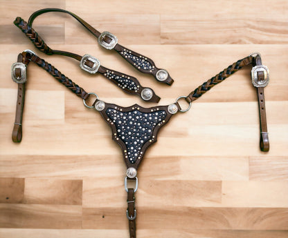 A cow leather headstall and breast collar set with black alligator pattern, clear rivets, and silver studs on a wooden surface.