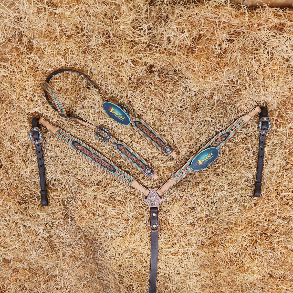 A tooled leather Western headstall and breast collar set with floral design, featuring topaz and black rivets, and antique copper hardware, laid out on a bed of straw.