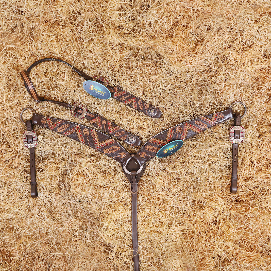 A Argentina cow leather horse bridle and breast collar set with red rivets and copper studs, displayed on a bed of straw.