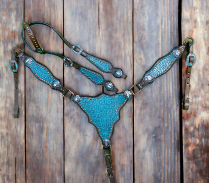 A Western headstall and breast collar set made of Argentina cow leather with teal alligator accents and copper stud embellishments, displayed on a wooden background.
